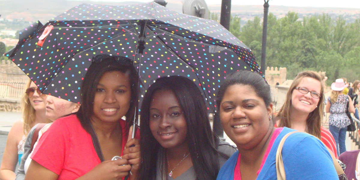 Three students in Spain with umbrella.