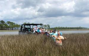 students wading through marsh grass after getting off of a boat