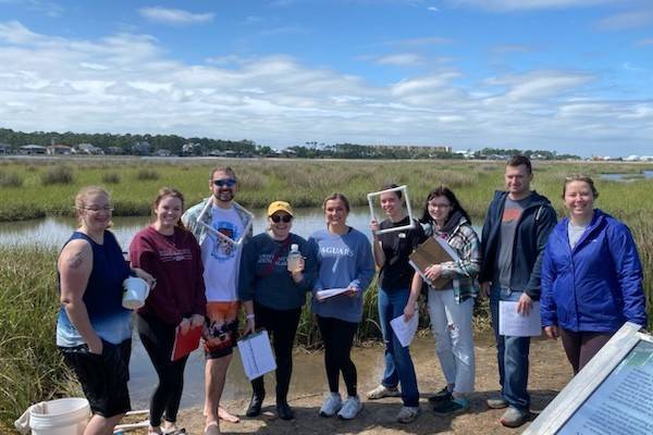 students holding field sampling equipment while standing in a marsh