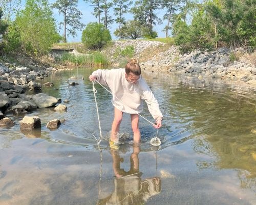 student standing in shallow creek with sampling net