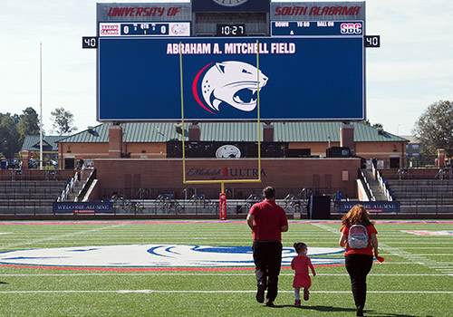 Alumni family running on the football field.