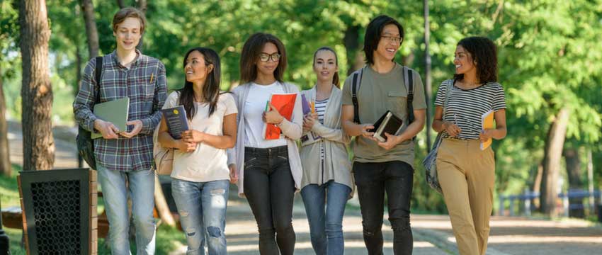 Students walking and talking carrying books outside 