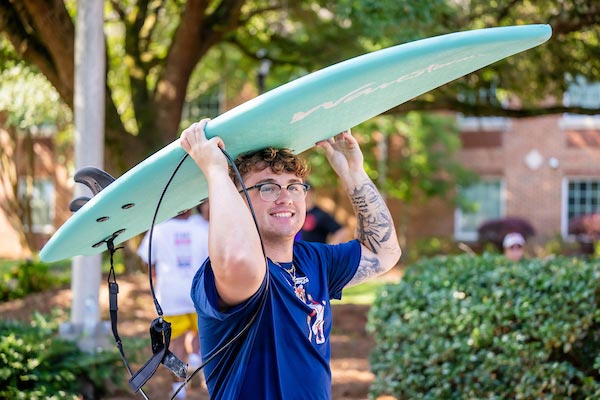 Student holding a surf board moving in.