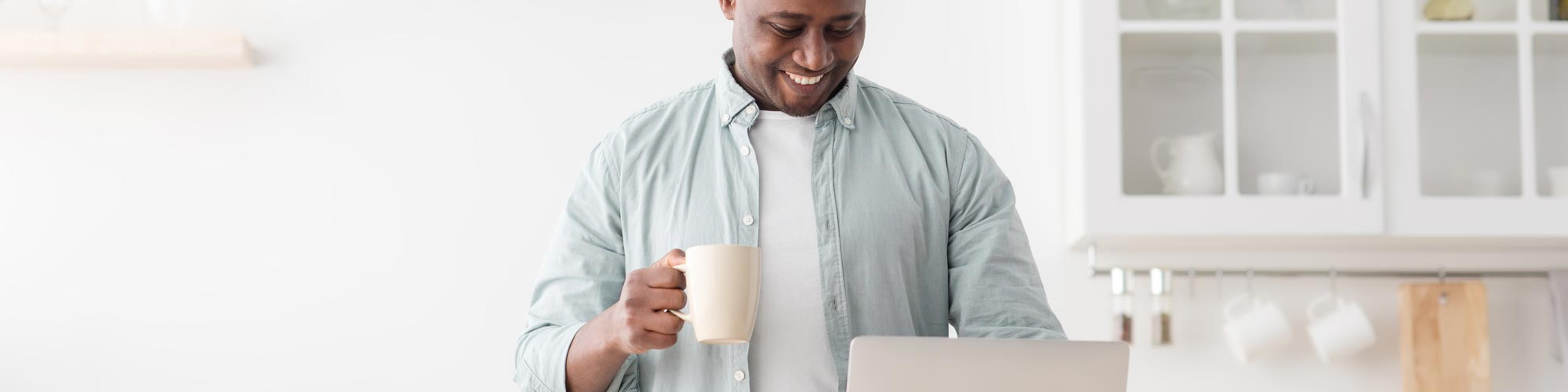 Man looking at laptop holding a mug in his hand.